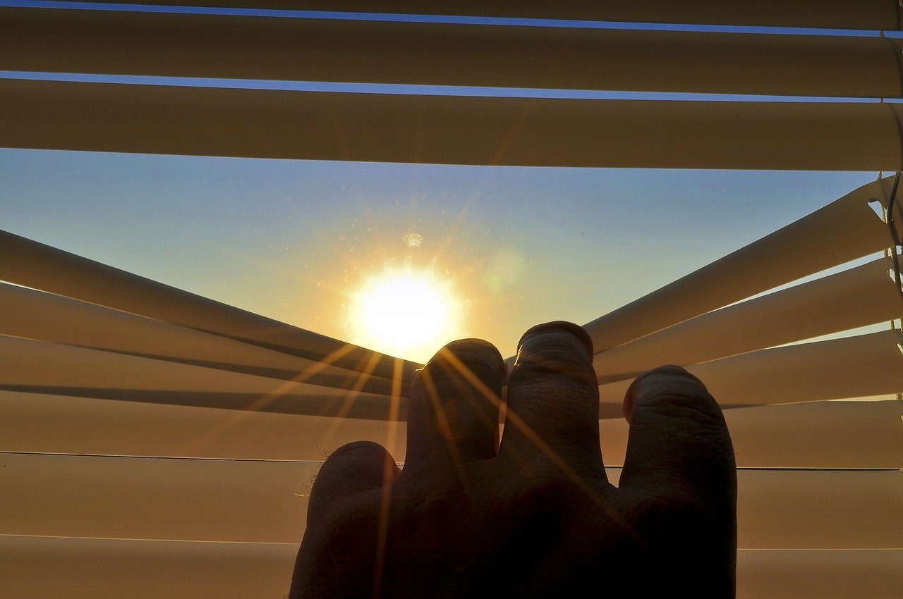 Persona al interior de su casa, observando el sol desde unas persianas.